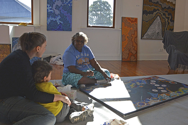 Artist Alma Nungurrayi Granites painting at Kate Owen Gallery and sharing her stories with two visitors to the gallery