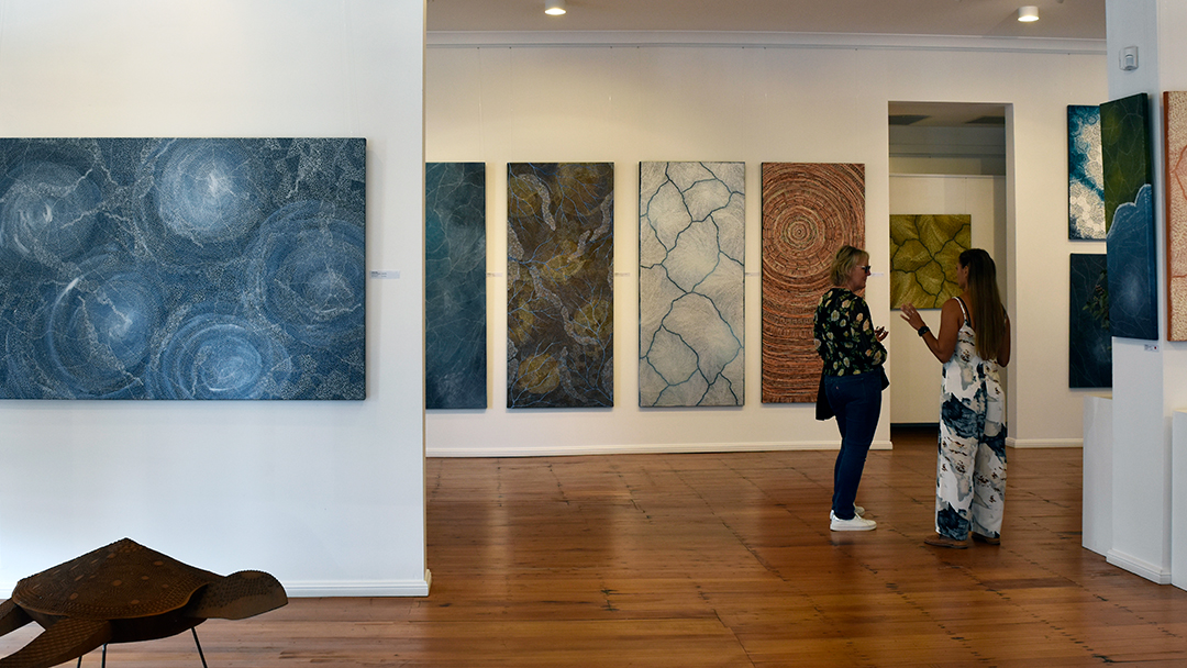Artist Sarrita King talking to a visitor to the gallery about her solo exhibition. Her artworks are surrounding them as they talk