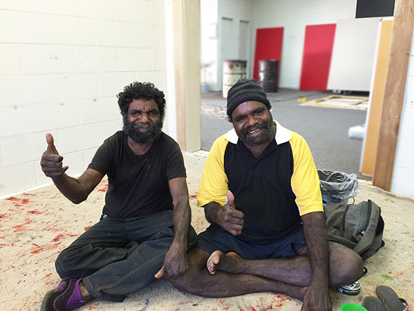 Artists Thomas and Walala Tjapaltjarri in the studio giving a 'thumbs up' gesture
