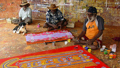 Three artists sitting cross legged on the floor, smiling, talking and painting.